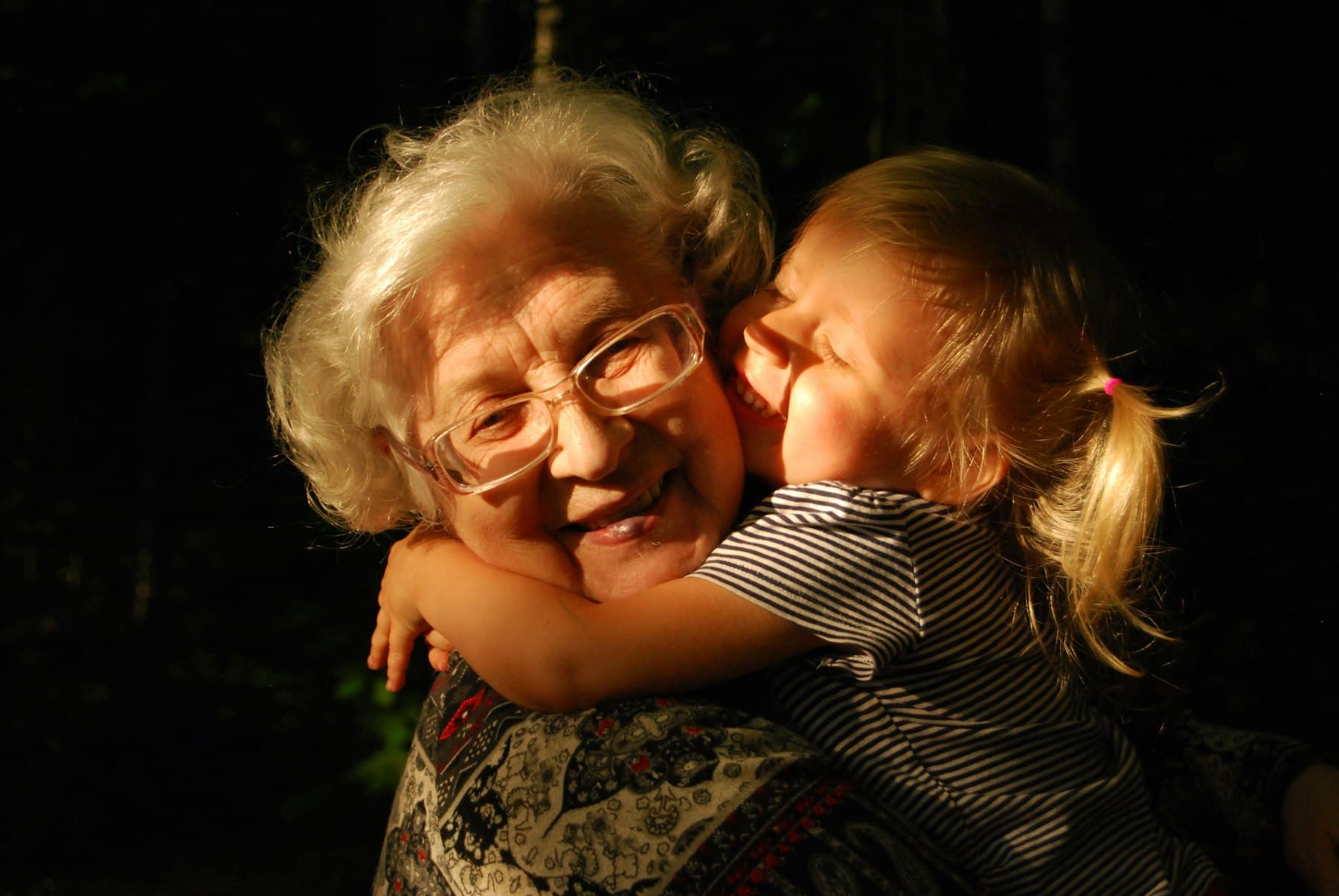 A grandmother laughing as her granddaughter hugs her
